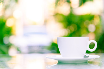 A white cup of coffee and silver spoon ready to served in the morning with relaxing and yellow lighting bokeh background.