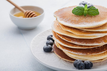 A stack of delicious pancakes with honey and blueberries on a light blue background