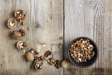 Walnut kernels in a  bowl and whole walnuts on table.