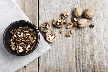 Walnut kernels in a  bowl and whole walnuts on table.