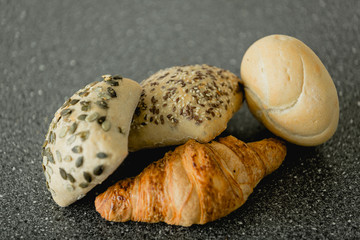 Fresh bakery products on the stone table: croissant, whole grain seed bread and a white bun.