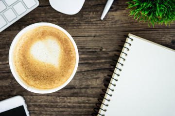 A latte coffee with art heart milk on the brown wood desk table from top view and copy space. Flat lay with desk, business and valentine concept.