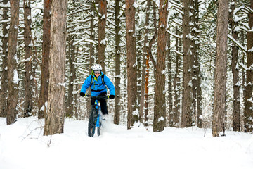 Fototapeta na wymiar Cyclist in Blue Riding the Mountain Bike in Beautiful Winter Forest. Extreme Sport and Enduro Biking Concept.