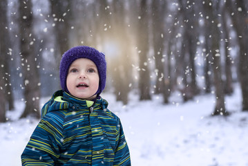 Little boy looks in the sky at the falling snow