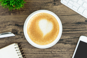 A latte coffee with art heart milk on the brown wood desk table from top view and copy space. Flat lay with desk, business and valentine concept.