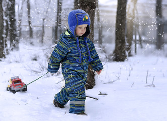 A little cheerful boy 2 years old in a blue jacket walks in the winter park