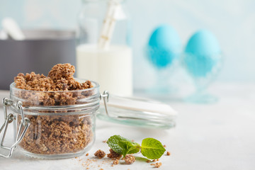 Chocolate baked granola in a glass jar with milk, eggs . Healthy breakfast concept, blue background