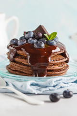 Chocolate pancakes with chocolate syrup, milk and blueberries. Blue background, breakfast concept, copy space