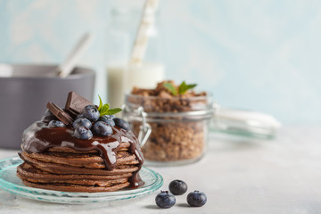 Chocolate pancakes with syrup and berries, chocolate granola and milk. Breakfast concept, blue background, copy space