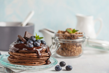 Chocolate pancakes with syrup and berries, chocolate granola and milk. Breakfast concept, blue background