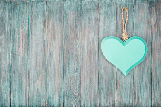 Wooden love heart hanging on vintage old grunge textured planks wall background. Retro style filtered photo