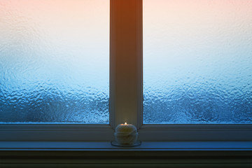 Frosted evening window with a candle burning