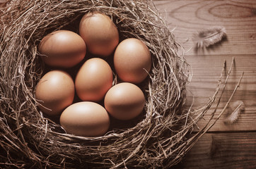 Still life with close-up view of raw chicken eggs in nest on rustic wooden background.