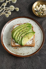 Avocado sandwich on dark rye toast bread made with fresh sliced avocado, cream cheese and seeds