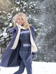 Winter lifestyle portrait of pretty girl throwing snow in the air. Smiling and having fun.