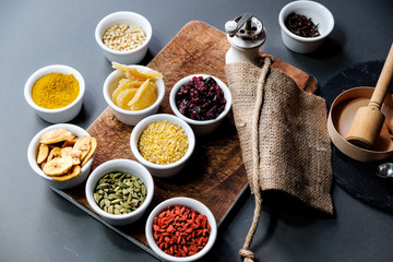 Various spices and herbs in a transparent bowl on black wooden background, top view