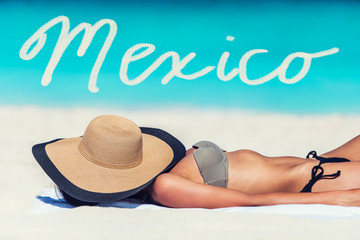 Mexico travel title written on beach vacation background. Word written over woman tanning lying down sleeping with hat on face for sun protection. Vacation girl relaxing on summer travel.