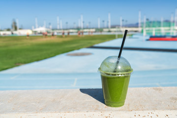 Green smoothie detox juice drink at outdoor sports stadium for runners athletes on blue running track. Healthy diet protein shake for sport people.