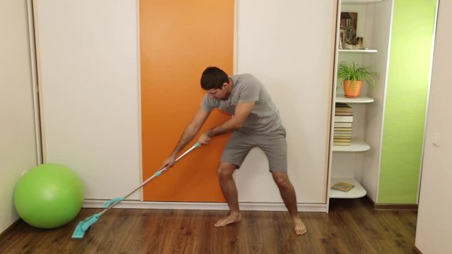 A man washes the floor with a mop and dances.