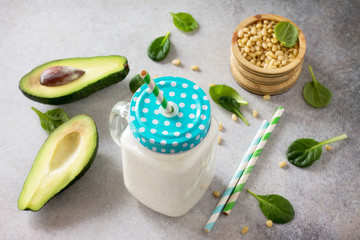 Mug Mason jar with a refreshing milkshake green spinach and pine nuts on a stone or slate background. Healthy vegetarian food.