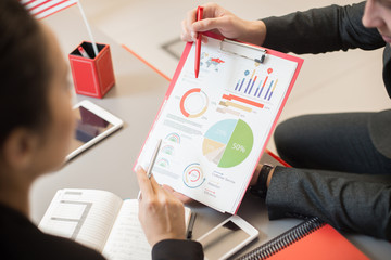High angle view at two business people discussing marketing statistics pointing at infographics with data charts during meeting in modern office