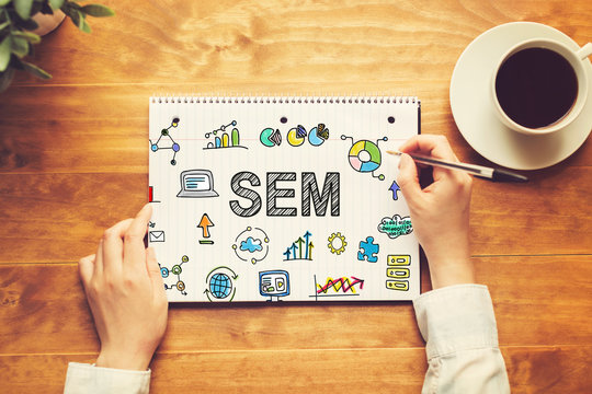 SEM text with a person holding a pen on a wooden desk