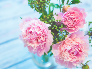 A bouquet of beautiful pink peonies on a bluish wooden table against soft-focused background.