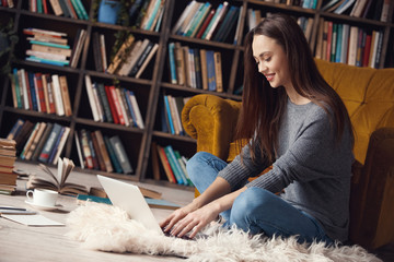 Young woman writer in library at home creative occupation sitting typing on laptop