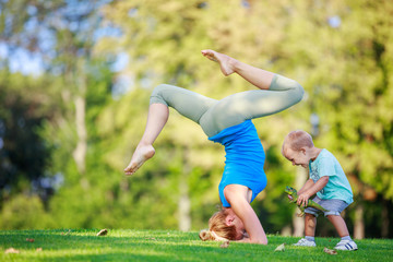Young woman working out outdoors, little son playing beside her