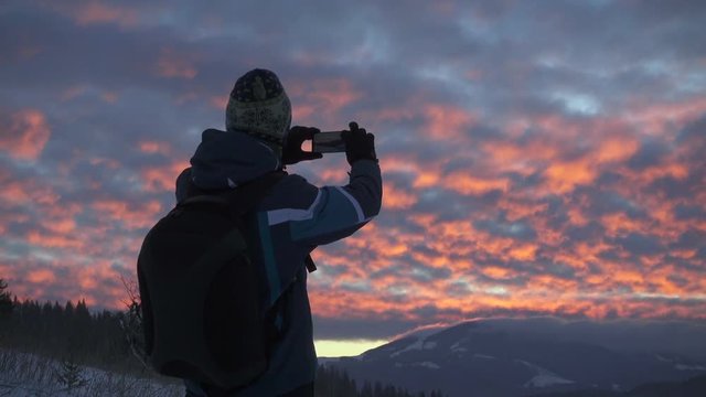 Tourist taking photograph of sunset in mountains