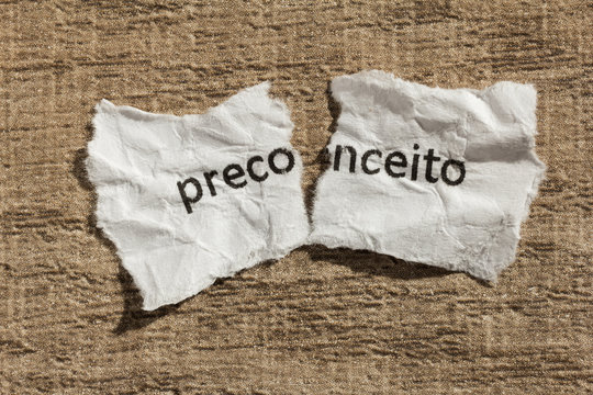 Torn paper written preconceito, portuguese word for prejudice, over wood table. Concept of old and abandoned idea or practice.