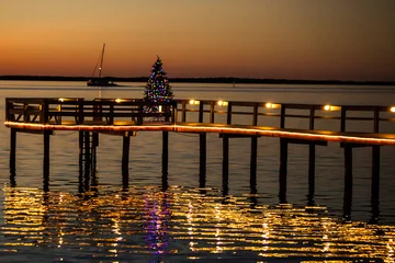 Printed roller blinds Pier A Dunedin, Florida pier lit with Chrismas lights and a Christmas tree at sunset with a sailboat cruising by in the background.