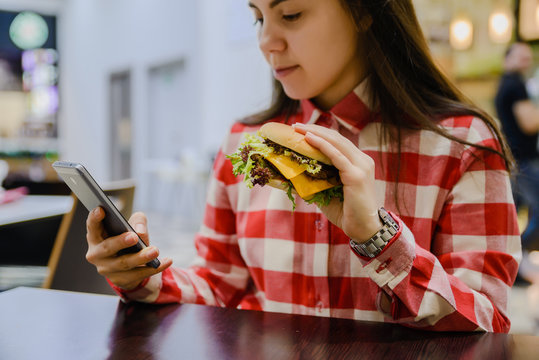 woman eat humburger while searfing the phone