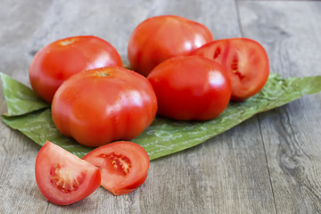 Ripe whole large tomatoes and a knife on a gray wooden background.