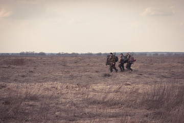 Group of men hunters gouing together through rural field in forward direction during hunting season
