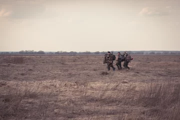 Crédence de cuisine en verre imprimé Chasser Group of men hunters gouing together through rural field in forward direction during hunting season