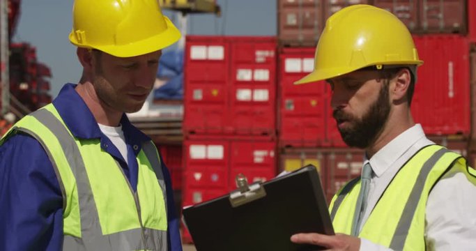 Dock workers shake hands and discuss shipping logistics in a shipyard. Shot on RED Epic.