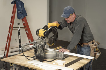 male carpenter wearing tool belt and cutting wood board with professional electric chop saw on work table on construction site