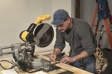 male carpenter wearing old tool belt, marking wood board with old square and pencil, next to...