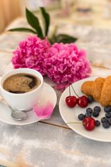 Morning coffee, croissant, blueberries and beautiful pink peony flowers on light table top view. Cozy breakfast on Mother or Woman day.