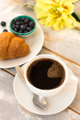 Morning coffee, croissant, blueberries and beautiful yellow peony flowers on light table top view. Cozy breakfast on Mother or Woman day.