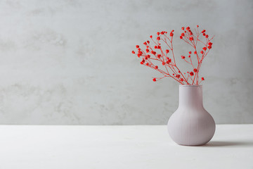 Small Bouquet of Red Flowers in Vintage Vase on White Table Grey Cement Wall Background. Styled...