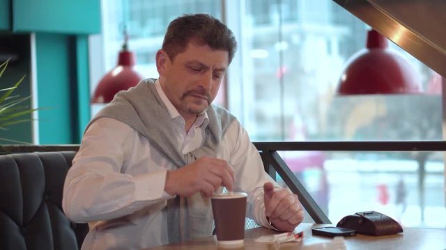 Man mature in a white shirt with sweater stirs sugar with a stick in the freshly made morning coffee
