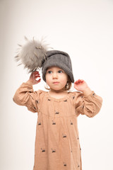 Portrait of pensive little girl. Cute little girl in beige dress in a gray hat isolated on white background.