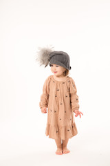 Portrait of happy little girl. Cute little girl in beige dress in a gray hat isolated on white background.