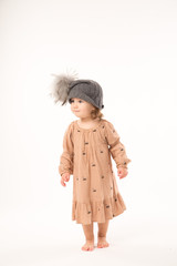 Portrait of happy little girl. Cute little girl in beige dress in a gray hat isolated on white background.