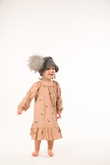 Portrait of happy little girl. Cute little girl in beige dress in a gray hat isolated on white background.