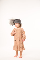 Portrait of happy little girl. Cute little girl in beige dress in a gray hat isolated on white background.
