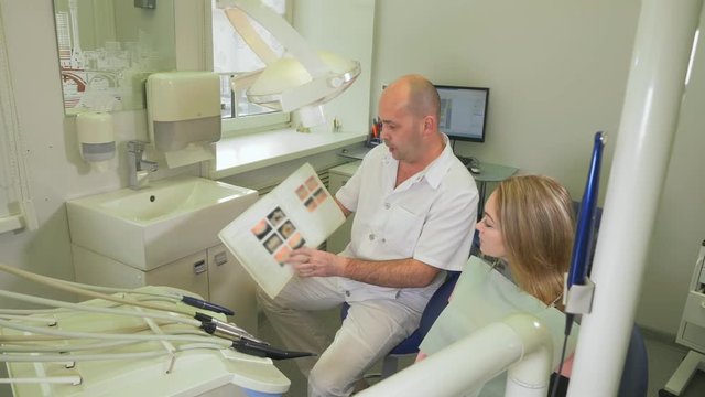 Professional look. Professional male dentist orthodontist checking teeth of his female client. The doctor shows the woman an album with photos of teeth, with examples of works.