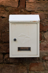 White metal mailbox on a red brick wall. Old brick wall. Mailbox covered with dust and dirt.